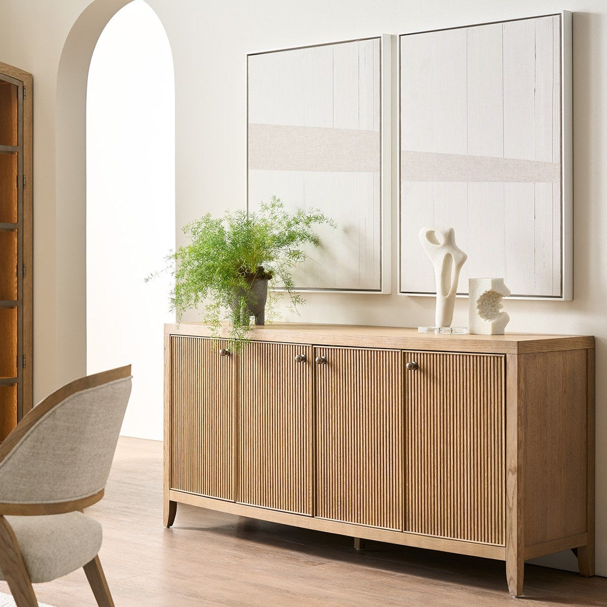 Wooden sideboard with decorative items in a room with a chair and mirror.