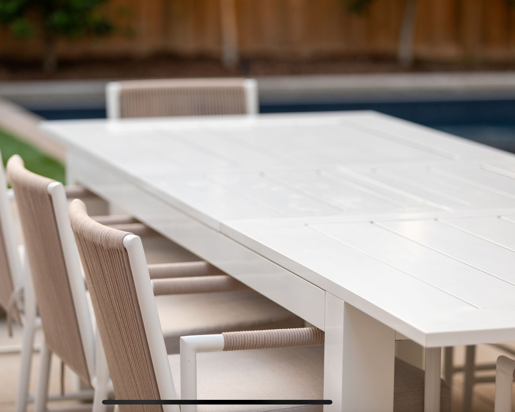 White outdoor dining table with chairs near a pool