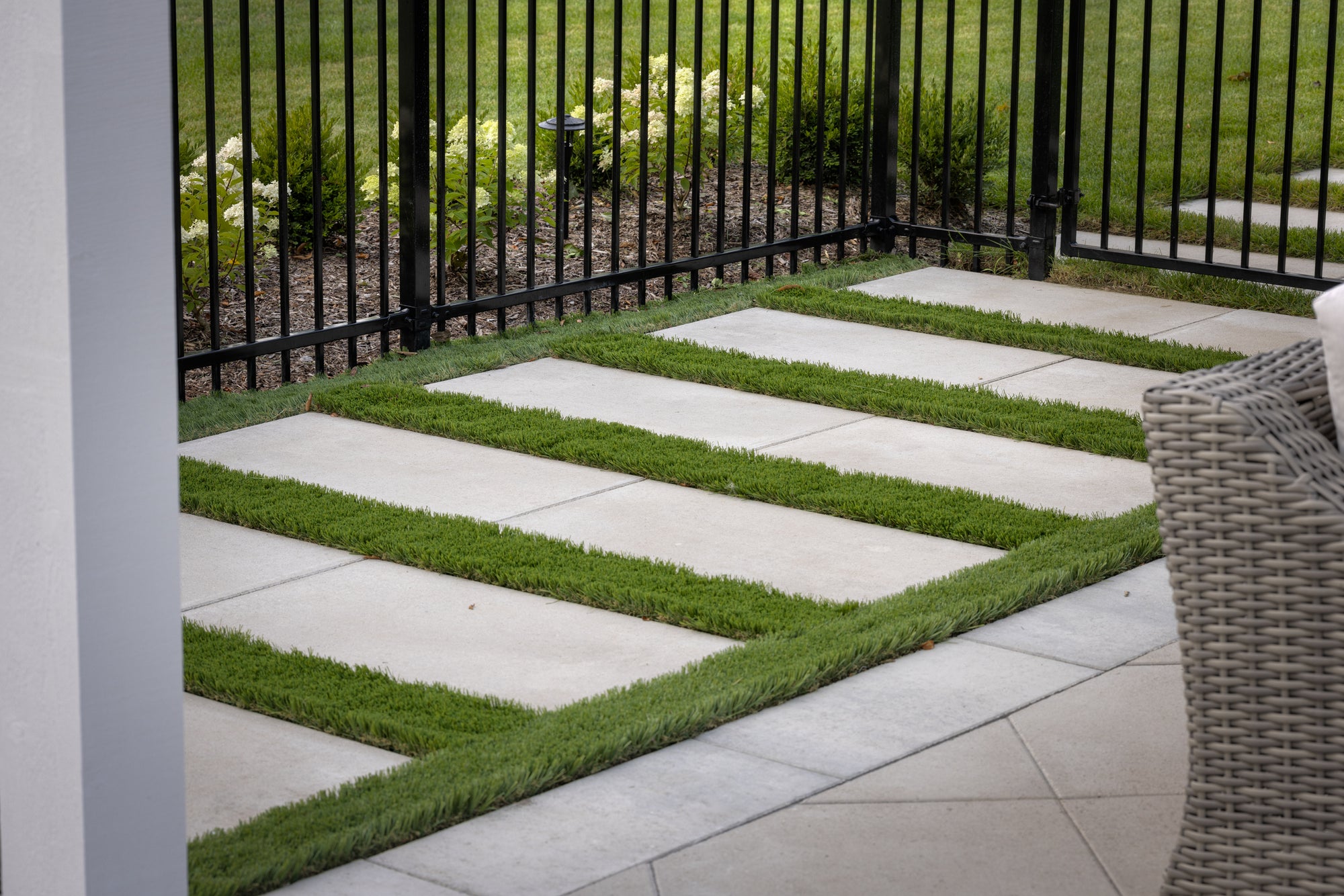Patio with stone tiles and grass patches, surrounded by a metal fence.