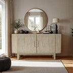 A beige sideboard with two doors, placed against a wall with a round mirror above it. The sideboard is accompanied by a lamp and decorative items on top.
