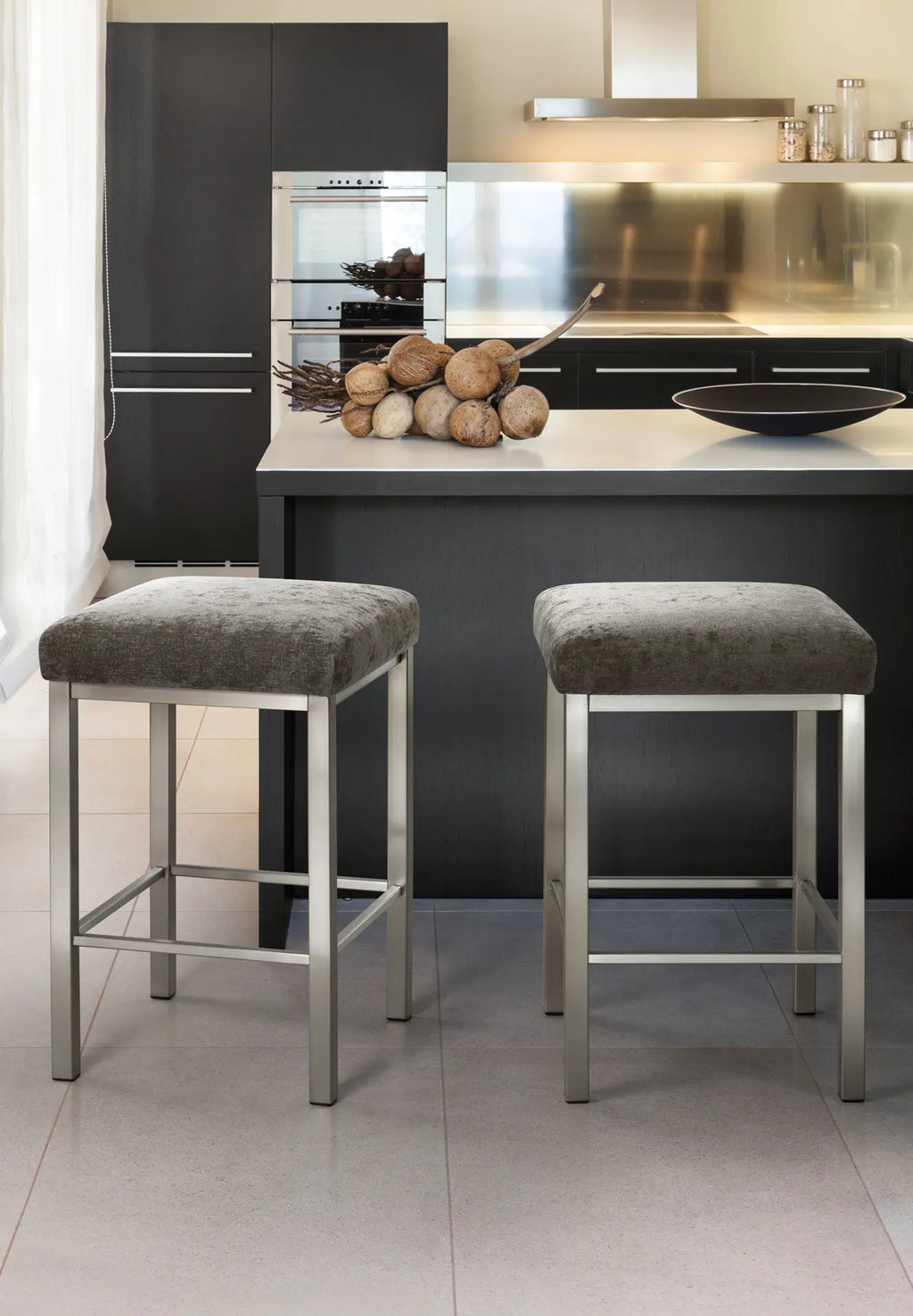Two gray bar stools in front of a kitchen island with a modern kitchen setup.