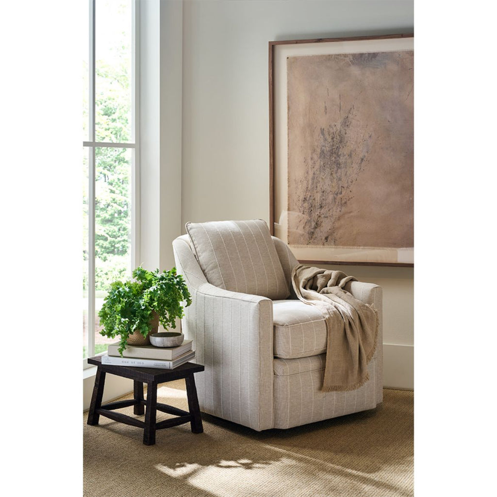 Beige swivel armchair in a room with a window, plant, and framed artwork.